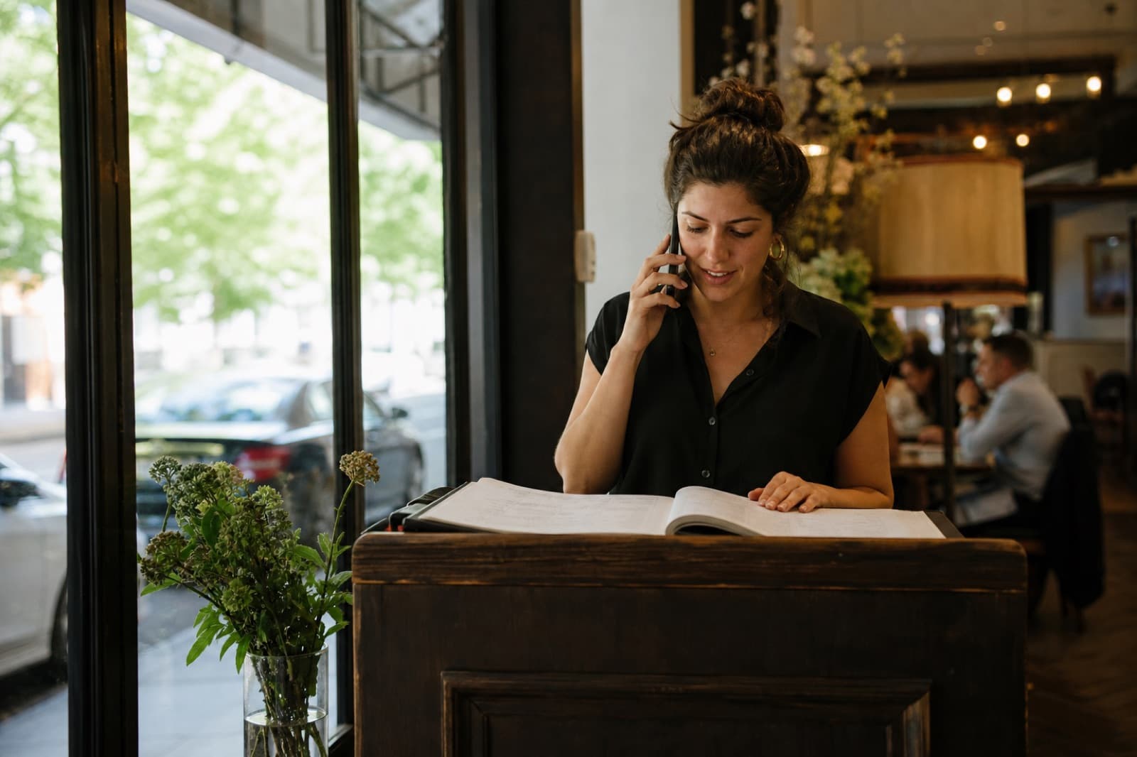 Someone at a restaurant host stand taking a call with the reservation book open.